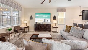 A modern living room with a sofa, coffee table, and a TV mounted on the wall. - Marvel Mansion! Championsgate Resort Shine Villas 9 Bedroom Villa (Davenport)