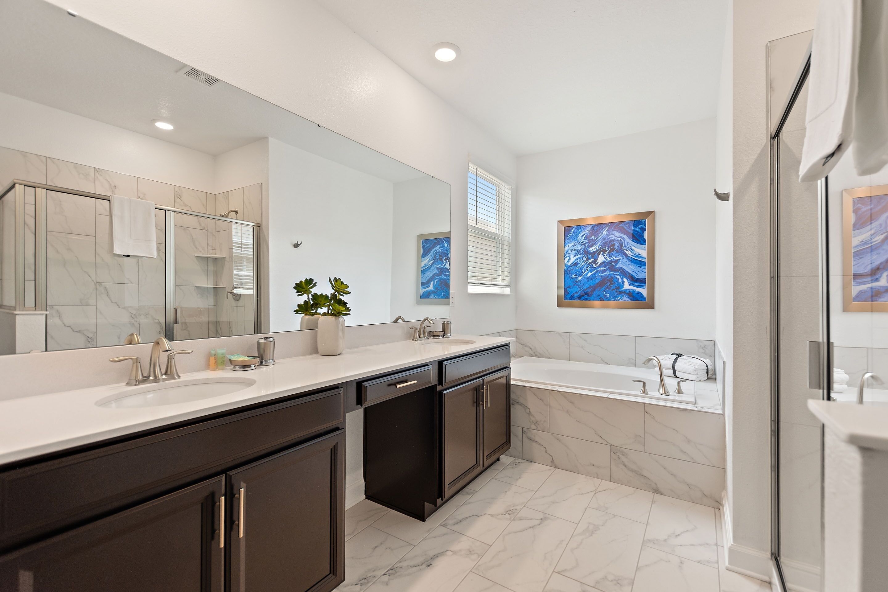 A modern bathroom with a large mirror, two sinks, a bathtub, and marble flooring.