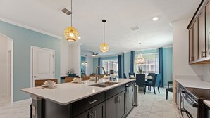 A modern kitchen with a large island, dark cabinetry, and pendant lighting. - Stars Align @ Storey Lake By Shine Villas 6 Bedroom Villa (Kissimmee)