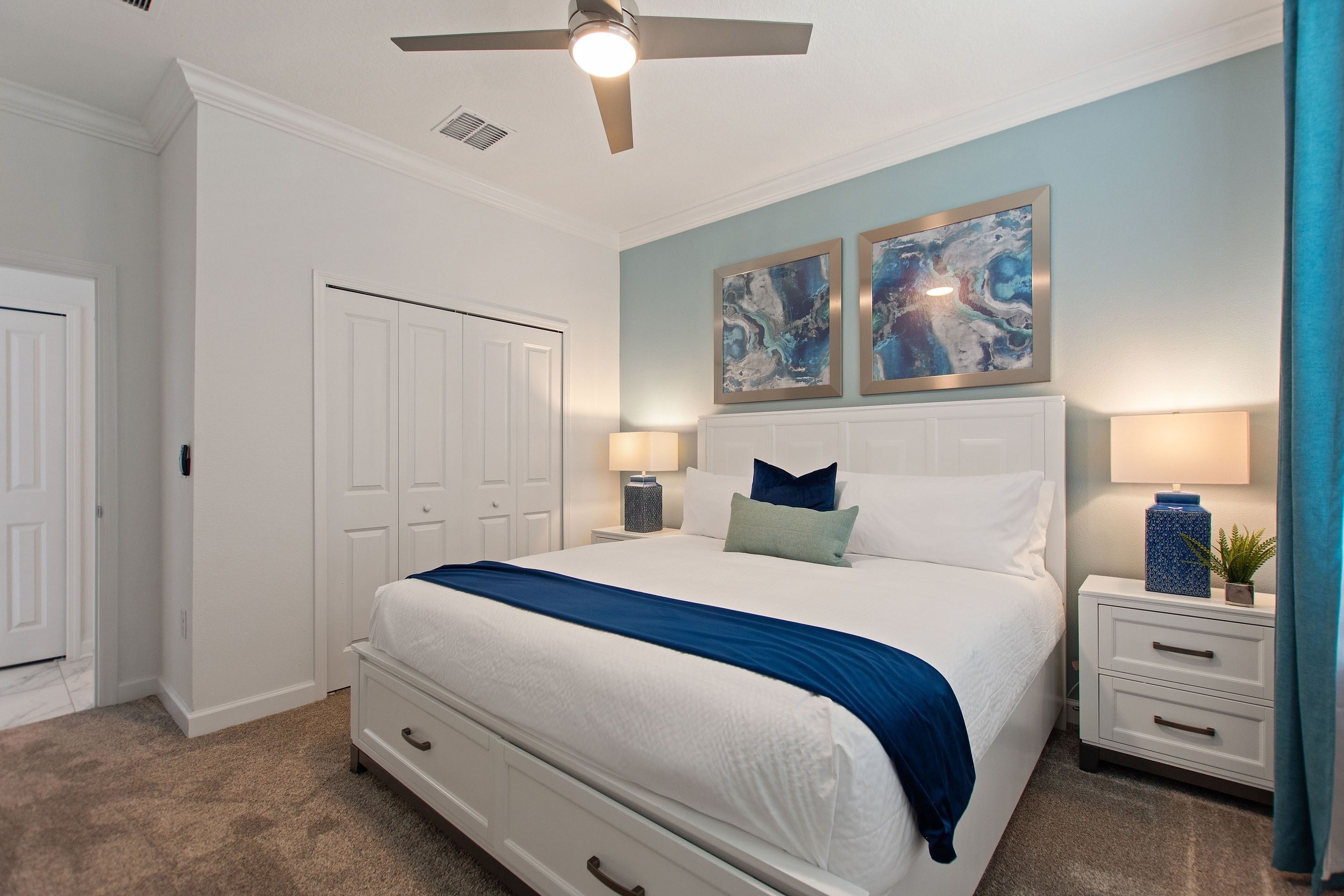 A bedroom with a bed, nightstands, a ceiling fan, and artwork on the wall.