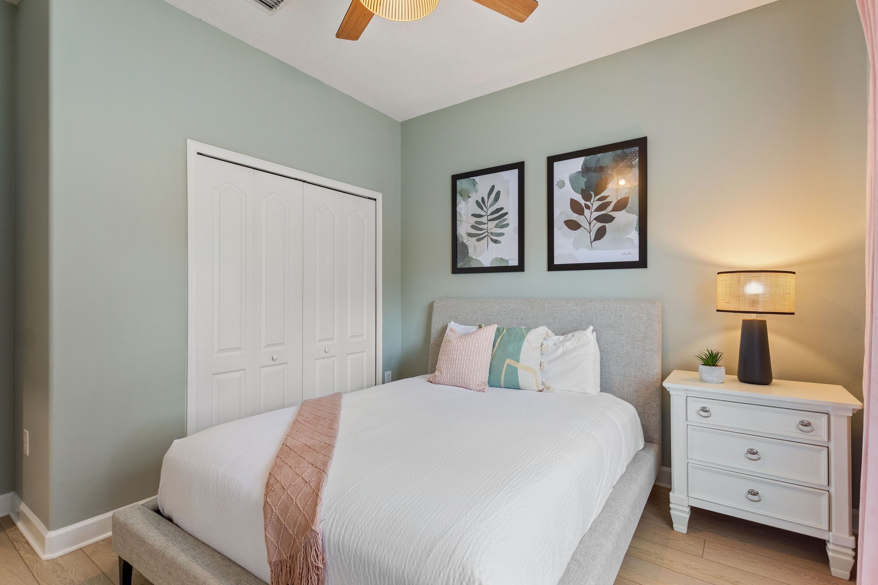 A bedroom with a bed, bedside table, lamp, and two framed pictures on the wall.