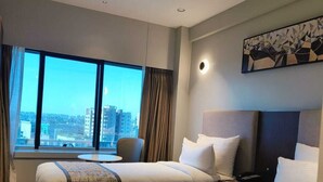 A hotel room with two beds, a city view, a round table, and a painting on the wall. - Ramee International Surat (Surat)