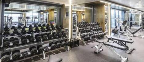 Un gimnasio con equipo de levantamiento de pesas, bancos y mancuernas.