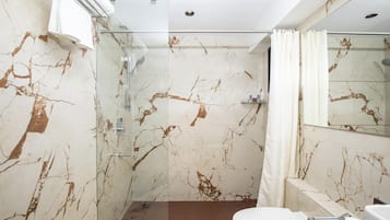 Un baño con cabina de ducha de vidrio, inodoro blanco y pared de mármol con vetas marrones.