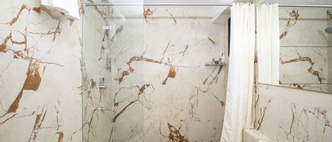 A bathroom with a glass shower enclosure, a white toilet, and a marble wall with brown veins.