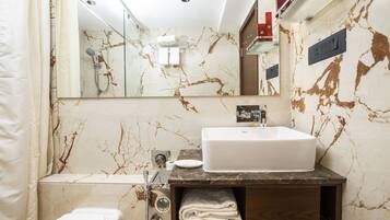A modern bathroom with a marble backsplash, a white sink, and a glass shower enclosure.