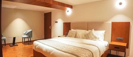 Una habitación de hotel moderna con una cama grande, una mesita de noche, una silla y una pequeña mesa.