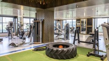 Un gimnasio con diferentes equipos de ejercicio, una llanta en el centro y amplios ventanales.