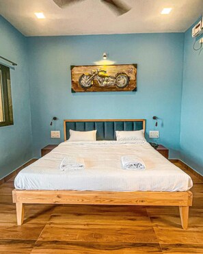 A bedroom with a large bed, wooden headboard, and a painting of a motorcycle on the wall. - Beach Village Resort (Shrivardhan)