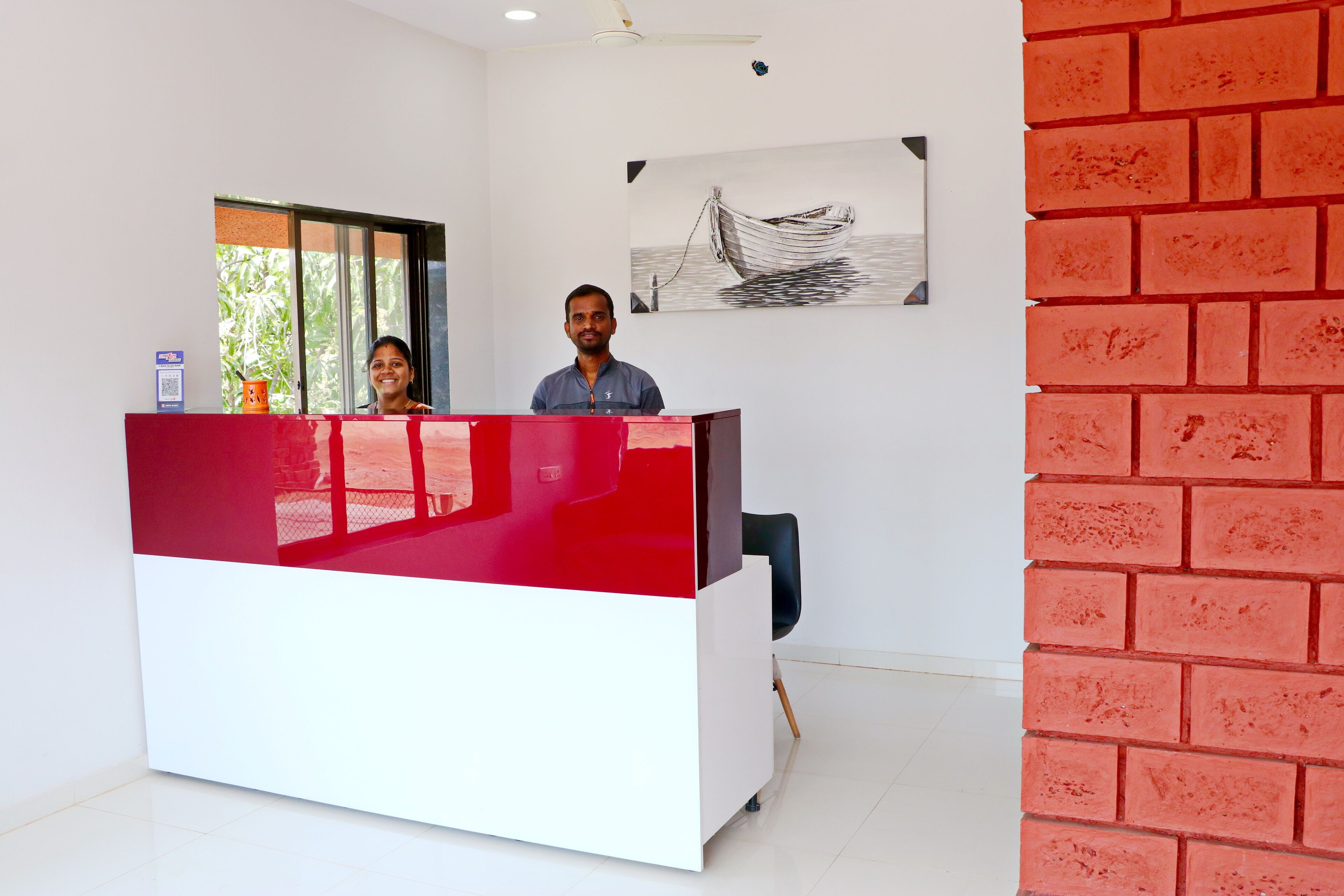 A reception desk with a red and white color scheme, a black chair, and a painting of a boat on the wall.