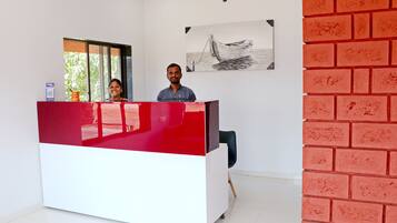 A reception desk with a red and white color scheme, a black chair, and a painting of a boat on the wall.