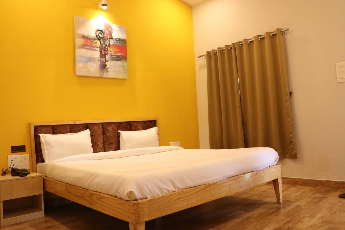 A hotel room with a wooden bed, a nightstand, a painting on the wall, and a window with curtains.
