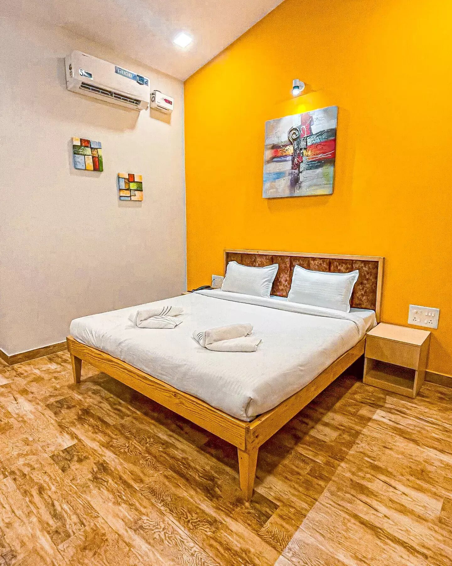 Ein Hotelzimmer mit einem hölzernen Bett, weißer Bettwäsche, einem Gemälde an der Wand und einer Klimaanlage.