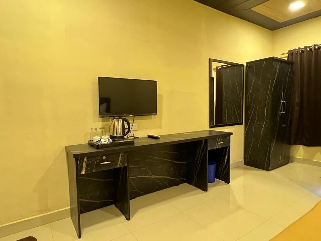 A hotel room with a black marble desk, a flat-screen TV mounted on the wall, and a large mirror above the desk.