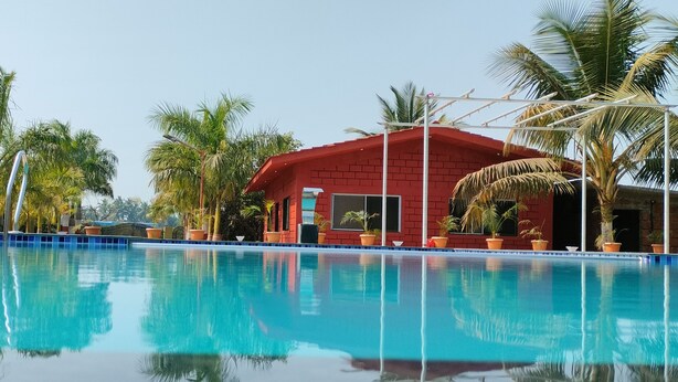 Ein klares Schwimmbecken mit Spiegelungen von Palmen und einem roten Gebäude im Hintergrund.