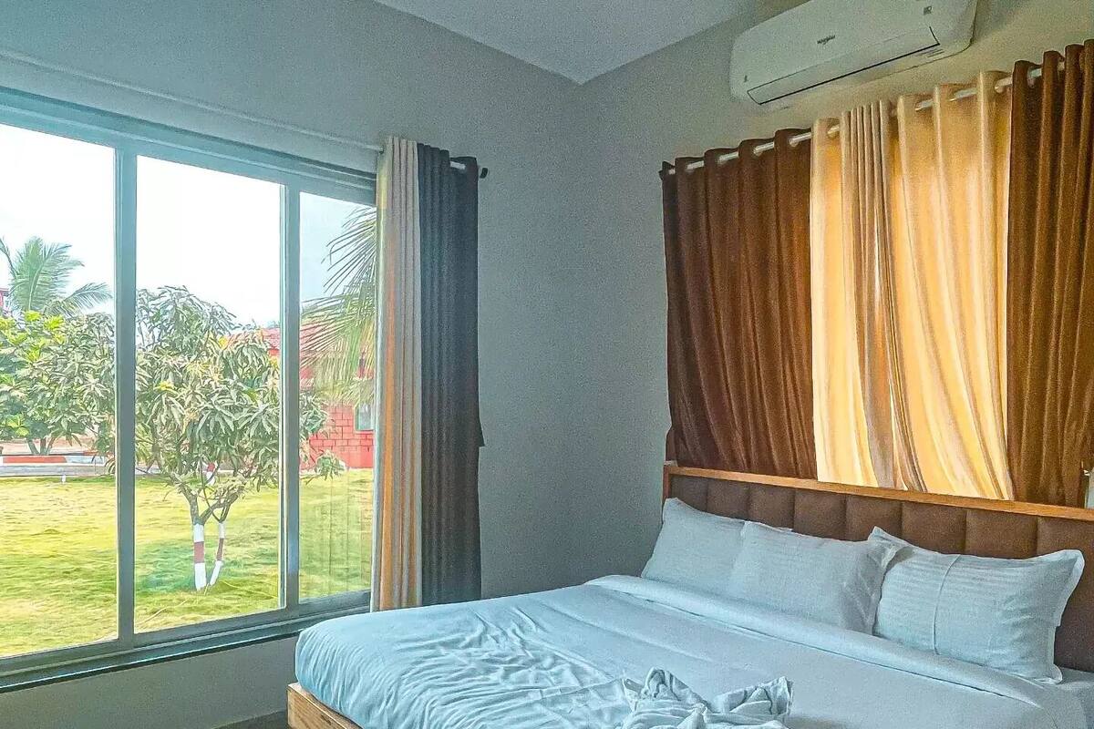A hotel room with a large bed, a window with curtains, and an air conditioning unit on the wall.