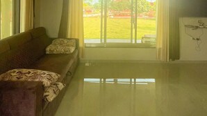 Ein geräumiges Wohnzimmer mit großem Fenster, einer Couch und einem Flachbildfernseher.