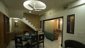 A modern kitchen with a dining area, a staircase, and a living room with a sofa and a TV. - Elis Hospitality Service Parth Bungalow (Ahmedabad)