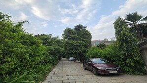 A paved pathway lined with dense greenery and parked cars. - Elis Hospitality Service Parth Bungalow (Ahmedabad)