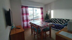 Ein Wohnzimmer mit Esstisch, Stühlen, einer Couch, einem Fernseher und einem Weihnachtsbaum.