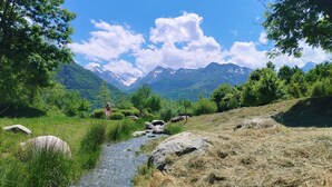 Eine Berglandschaft mit einem Bach, Bäumen und blauem Himmel.