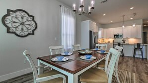 A dining area with a wooden table, white chairs, and blue bowls. A chandelier hangs above the table. - Spacious Gulfport Home - Walk to Beach! (Gulfport)