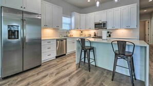 A modern kitchen with white cabinets, stainless steel appliances, and a bar area with stools. - Spacious Gulfport Home - Walk to Beach! (Gulfport)