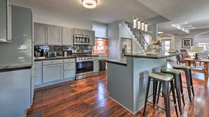 A modern kitchen with grey cabinets, stainless steel appliances, a central island with stools, and a staircase leading to another level. - 3 Mi to French Quarter: Family Home in New Orleans (New Orleans)