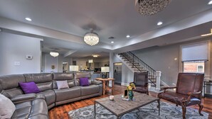 A spacious living room with a leather sofa, a coffee table, and a chandelier. A staircase leads to an upper level. - 3 Mi to French Quarter: Family Home in New Orleans (New Orleans)