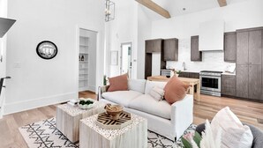 A spacious living area with a white sofa, wooden coffee table, and a kitchen with dark wooden cabinets and stainless steel appliances. - Serenbe, Palmetto, Ga, Escape, Serenity, Unforgettable, Scenic, Relaxation, New (Palmetto)