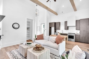 A spacious living area with a white sofa, wooden coffee table, and a kitchen with dark wooden cabinets and stainless steel appliances. - Serenbe, Palmetto, Ga, Escape, Serenity, Unforgettable, Scenic, Relaxation, New (Palmetto)