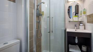 A modern bathroom with a glass-enclosed shower, a toilet, a sink with a mirror, and toiletries on the counter.