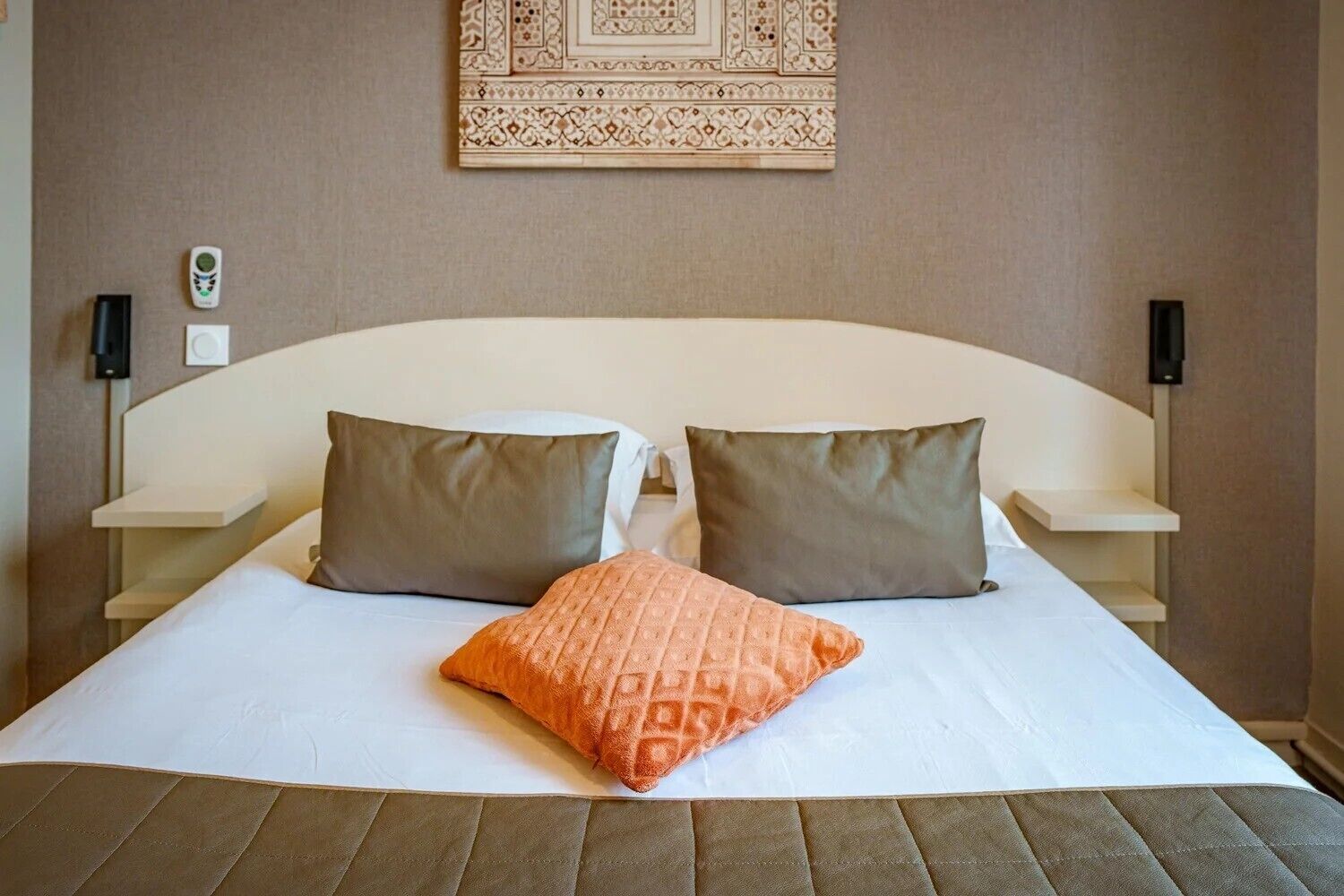 Een hotelkamer met een groot bed, twee nachtkastjes en een decoratief wandobject.