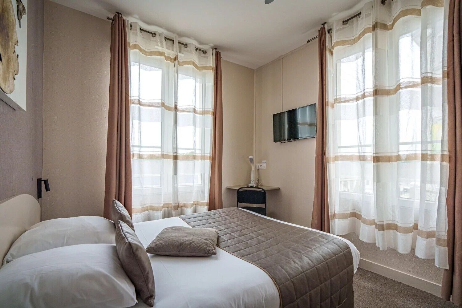 Et hotelværelse med en seng, et fjernsyn ophængt på væggen og et lille bord med en lampe.