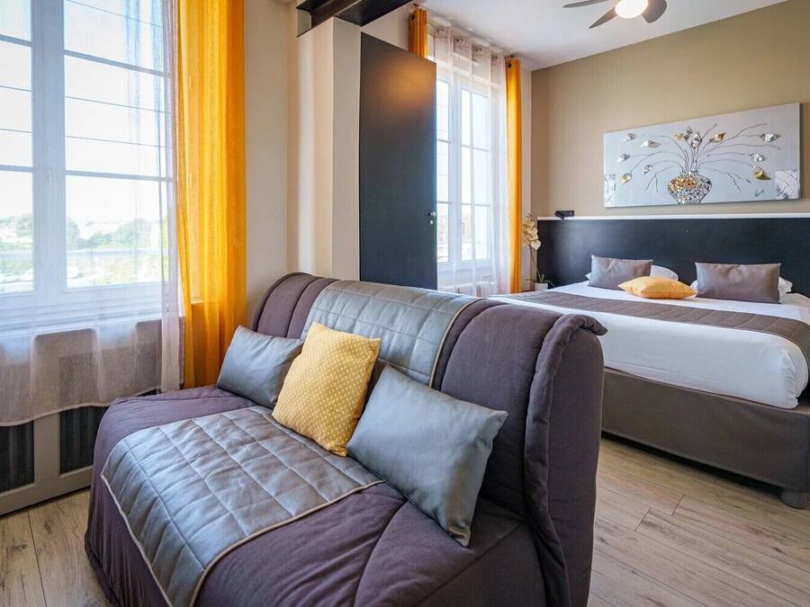 A modern hotel room with a large window, a sofa, a bed, and a painting on the wall.
