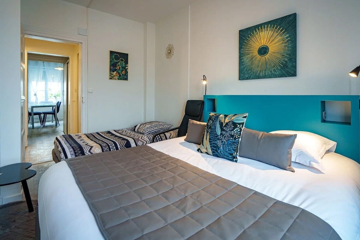 Une chambre d’hôtel avec un grand lit, un bureau et une chaise. Il y a un tableau au mur et une fenêtre donnant sur l’extérieur.
