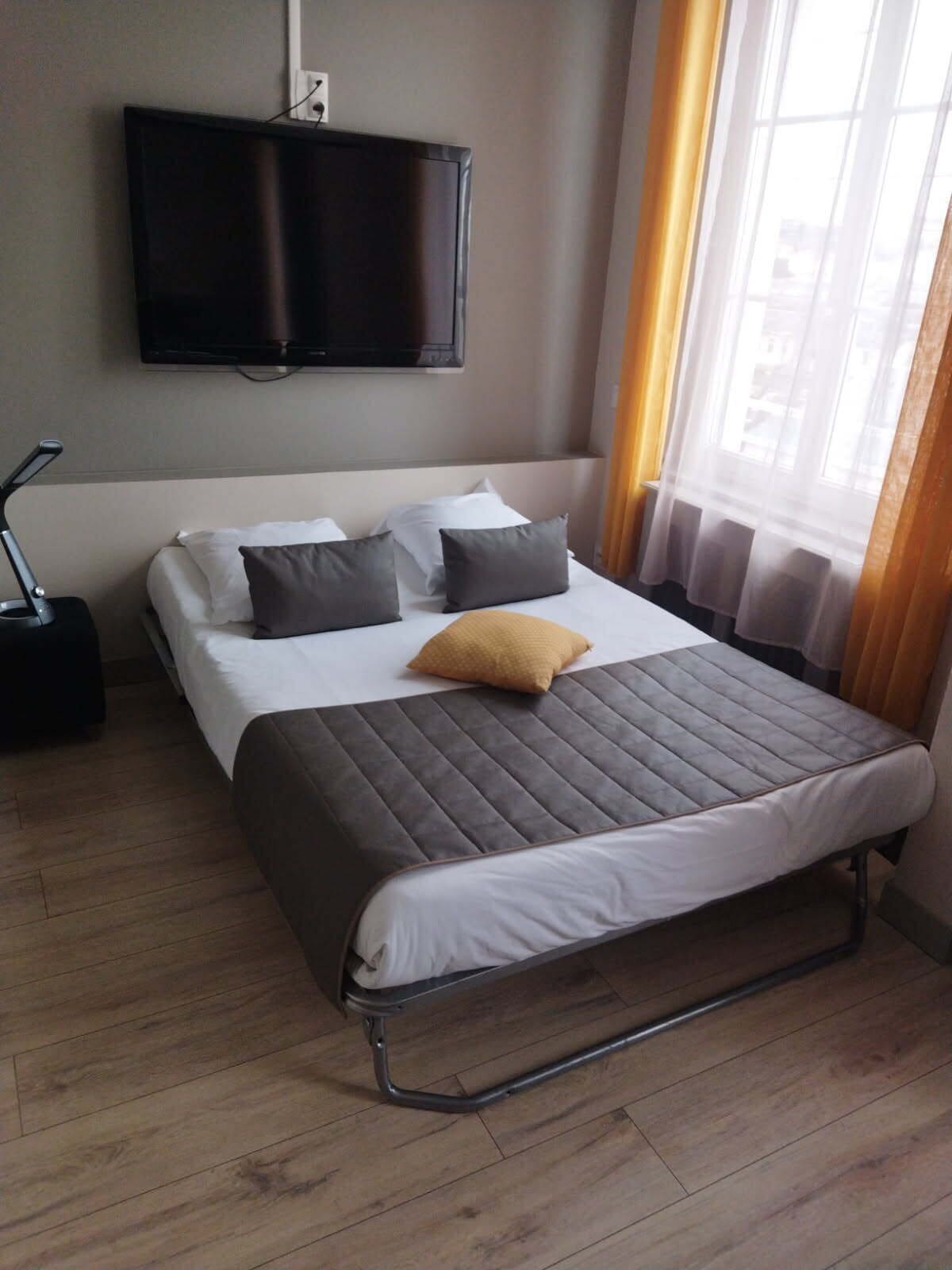 A hotel room with a bed, a TV mounted on the wall, a suitcase, and a window with curtains.