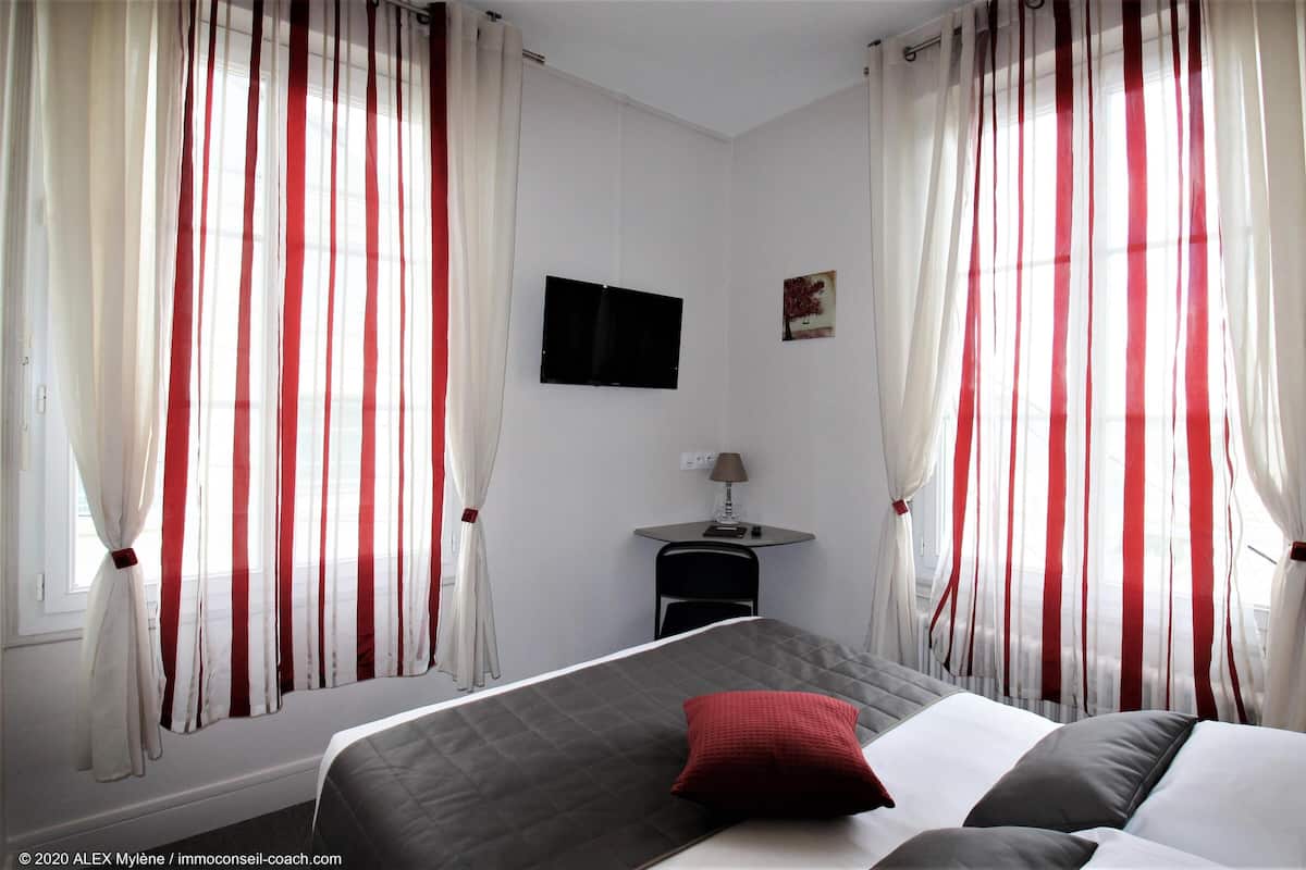 Une chambre d’hôtel avec un lit, une petite table avec une lampe et des rideaux à rayures rouges et blanches.