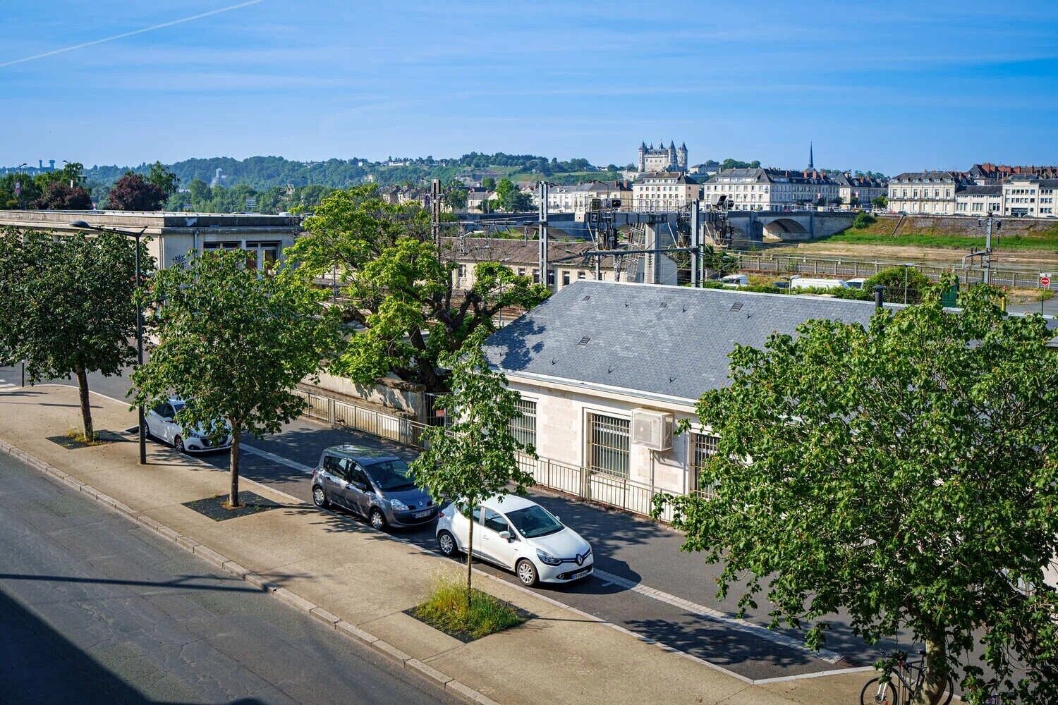 Vista de la calle con coches estacionados, árboles y edificios al fondo.