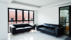 Un salon moderne avec deux canapés en cuir noir, une grande fenêtre donnant sur un immeuble en briques et une plante en pot.