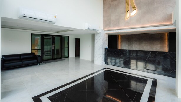 Un hall d’entrée moderne avec un comptoir de réception en marbre, un sol carrelé en noir et blanc et un canapé noir.