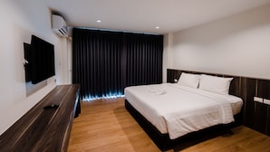 Une chambre d’hôtel moderne dotée d’un grand lit, d’un téléviseur à écran plat fixé au mur et d’un rideau sombre en arrière-plan.
