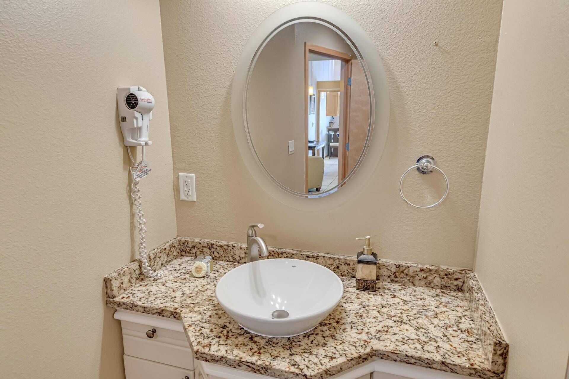 Une salle de bain avec un lavabo blanc, un miroir rond, un sèche-cheveux et un porte-serviettes.