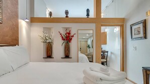 Une chambre d’hôtel avec un grand lit, deux vases de fleurs, un miroir et un tableau encadré au mur.