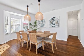 Un coin repas avec une table en bois, des chaises en osier et des lampes suspendues.