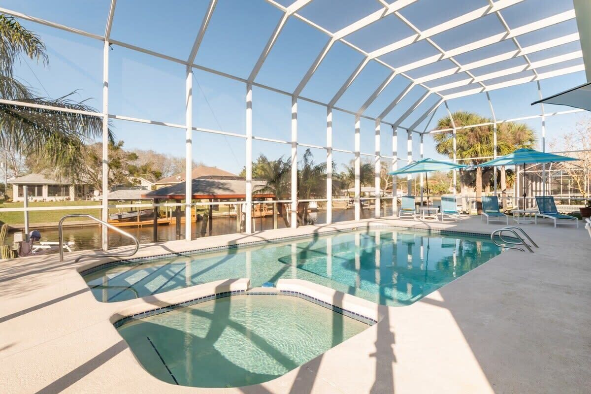 Uma área de piscina com estrutura de vidro, espreguiçadeiras e guarda-sóis.