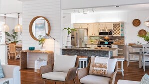 Une cuisine moderne avec des meubles blancs, un îlot central et un coin repas doté de chaises en osier.