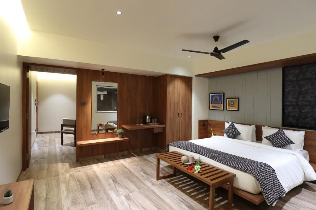 A modern hotel room with a large bed, wooden furniture, a ceiling fan, and a small seating area.