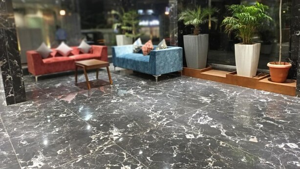 Un vestíbulo con suelo de mármol, un sofá rojo, un sofá azul y plantas en macetas.