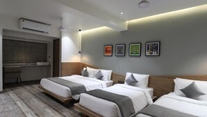 Una habitación de hotel con tres camas, un escritorio y un ventanal grande.
